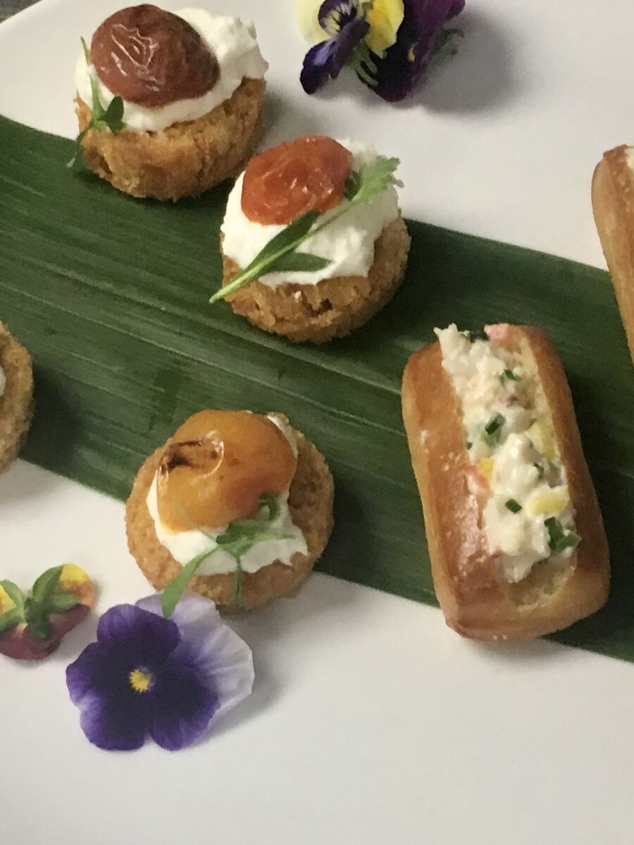 Goat cheese and confit tomato profiteroles and mini-brioche lobster rolls on a banana leaf with edible flowers